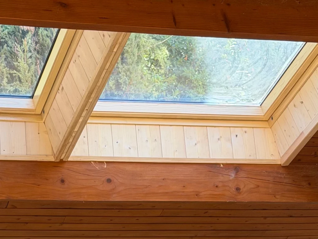 Vue intérieure d'une verrière jumelée VELUX intégrée dans une toiture avec charpente et poutres en bois massif.