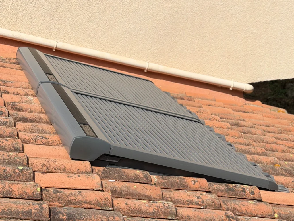 Vue latérale de volets roulants solaires VELUX fermés sur une toiture en tuiles pour une protection thermique optimale.
